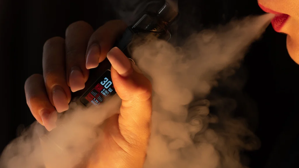 Mulher usando vape, dando um trago e exalando fumaça, ilustrando efeitos na laringe e voz