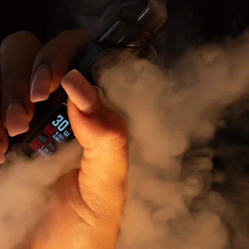 Mulher usando vape, dando um trago e exalando fumaça, ilustrando efeitos na laringe e voz